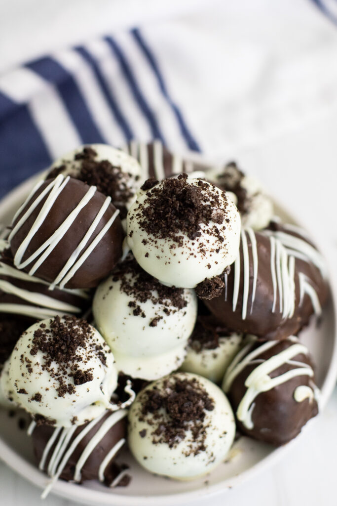 An overhead view of a pile of chocolate and white chocolate covered Oreo truffles on a small plate sitting on a linen napkin.