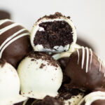 A pile of Oreo truffles with the top, white chocolate covered truffle with a bite taken out of it.