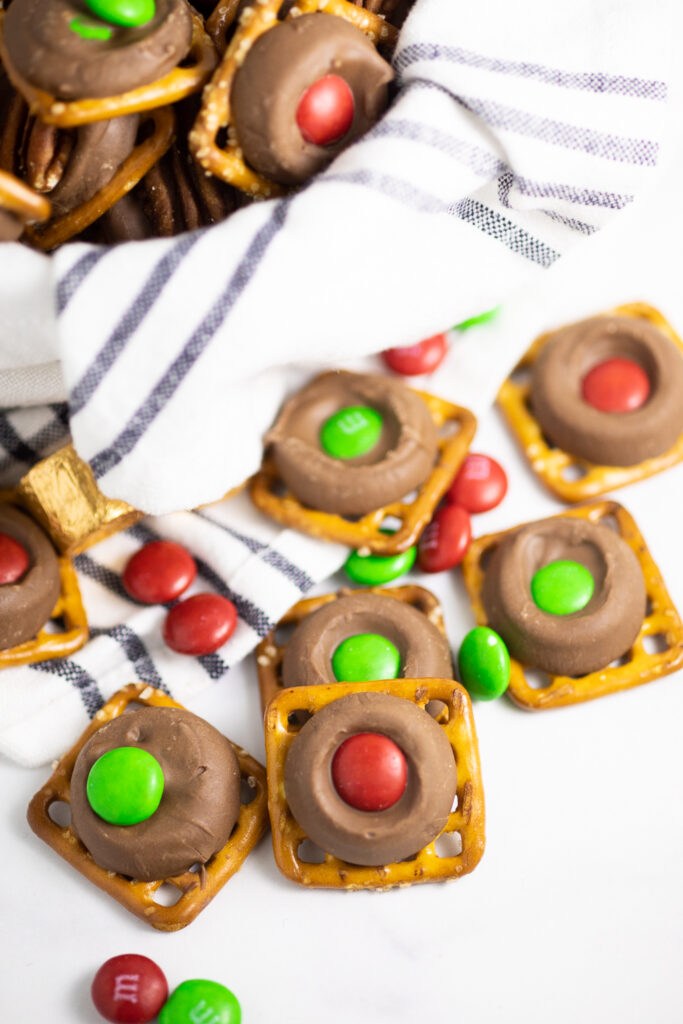 Rolo pretzels scattered on a white marble background with red and green M&M's scattered around them and rolos in gold foil wrappers behind.