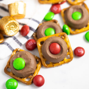 Rolo pretzels scattered on a white marble background with red and green M&M's scattered around them and rolos in gold foil wrappers behind.