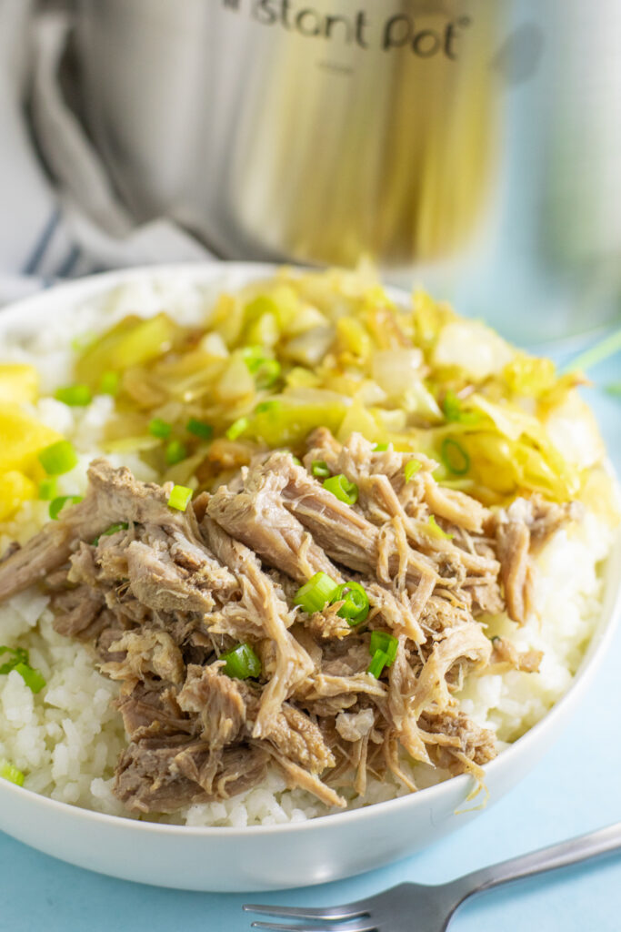 A shallow bowl filled with white rice and topped with Instant Pot Kalua Pork topped with sliced green onions on top.