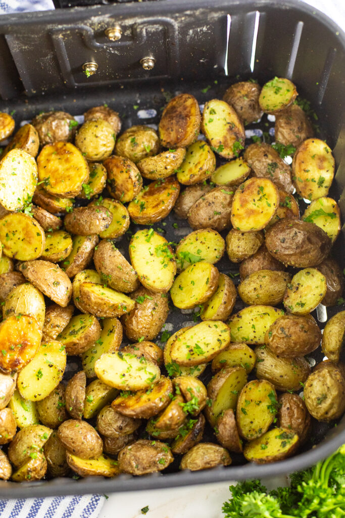 A square air fryer basket filled with halved crispy baby potatoes topped with fresh parsley.