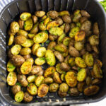 A square air fryer basket filled with halved crispy baby potatoes topped with fresh parsley.