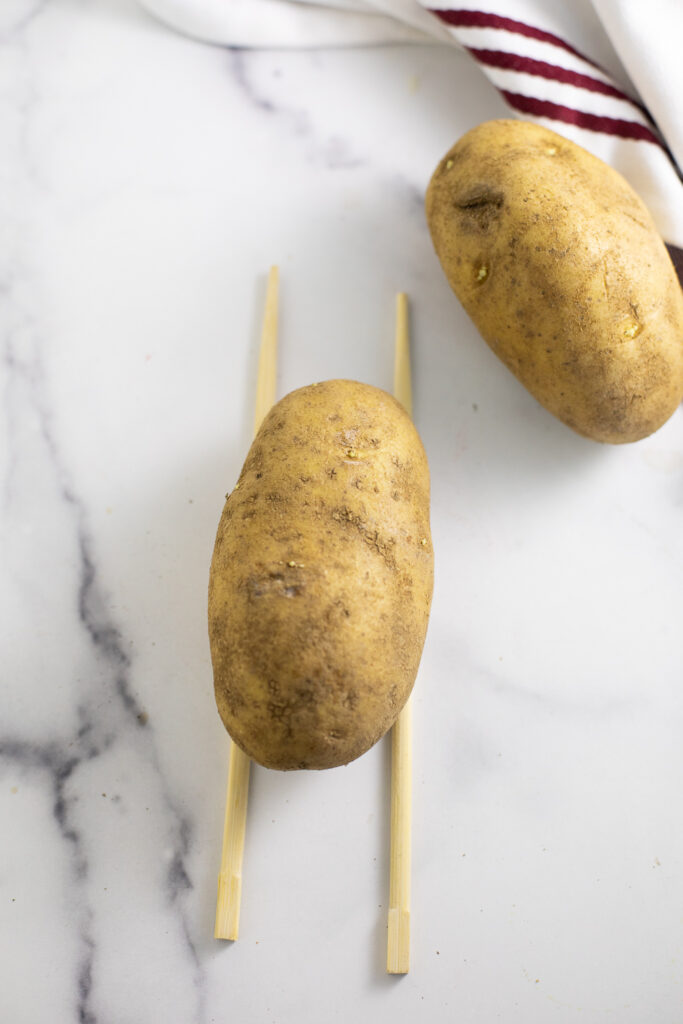 Potato with wooden chopsticks on either side on a white marble counter top.