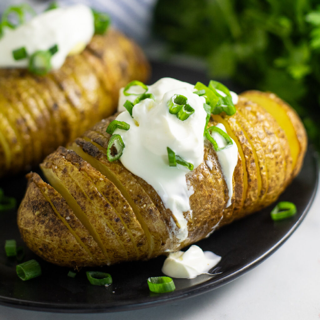 Air fryer hasselback potato topped with sour cream and green onions.
