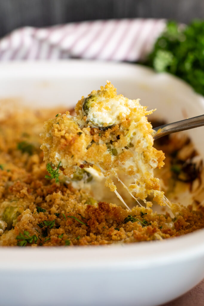 A spoon scooping up a large portion of cheesy brussels sprouts gratin with the cheese pulling from the dish.