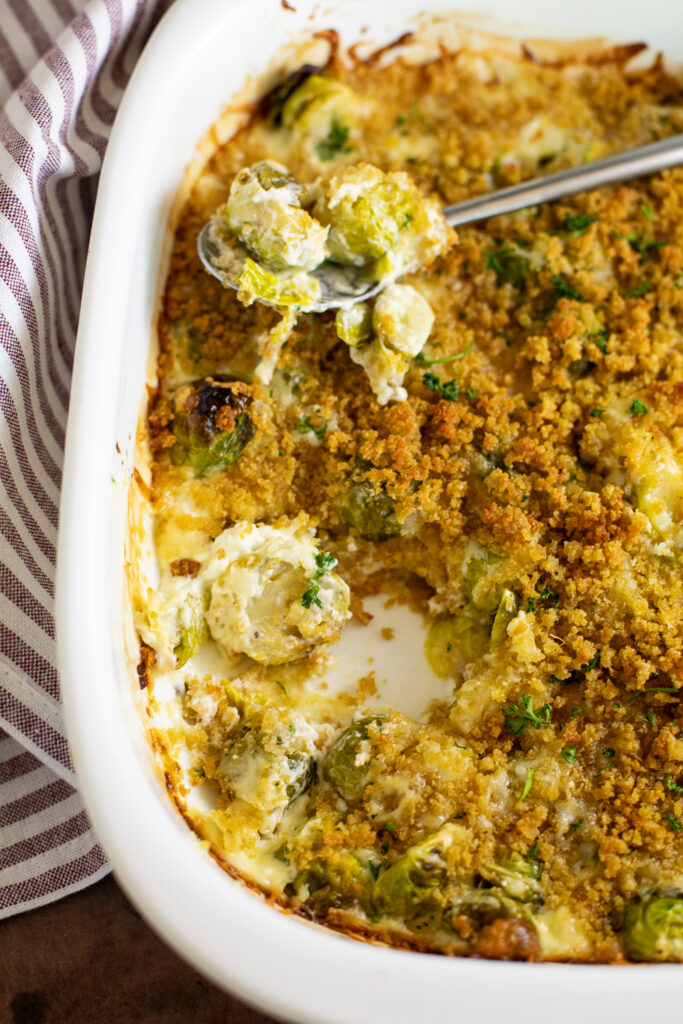 Casserole dish with a scoop of brussels sprouts gratin missing and a spoon sitting on top of the dish.