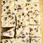 An overhead view of cranberry Bliss Bars cut into triangles and lined up on a wooden cutting board.