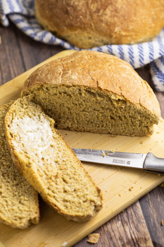 Half a loaf of Swedish limpa bread with two slices of the same bread smeared with butter on a cutting board next to a sharp knife.