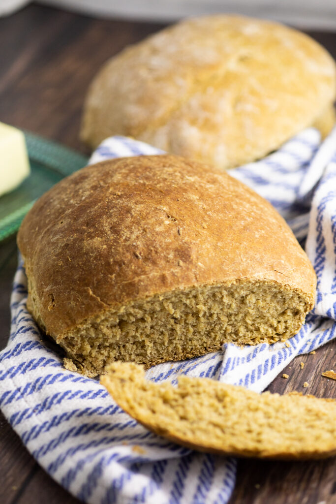 A loaf of Swedish limpa bread with a slice cut off laying in the front on a striped linen napkin.