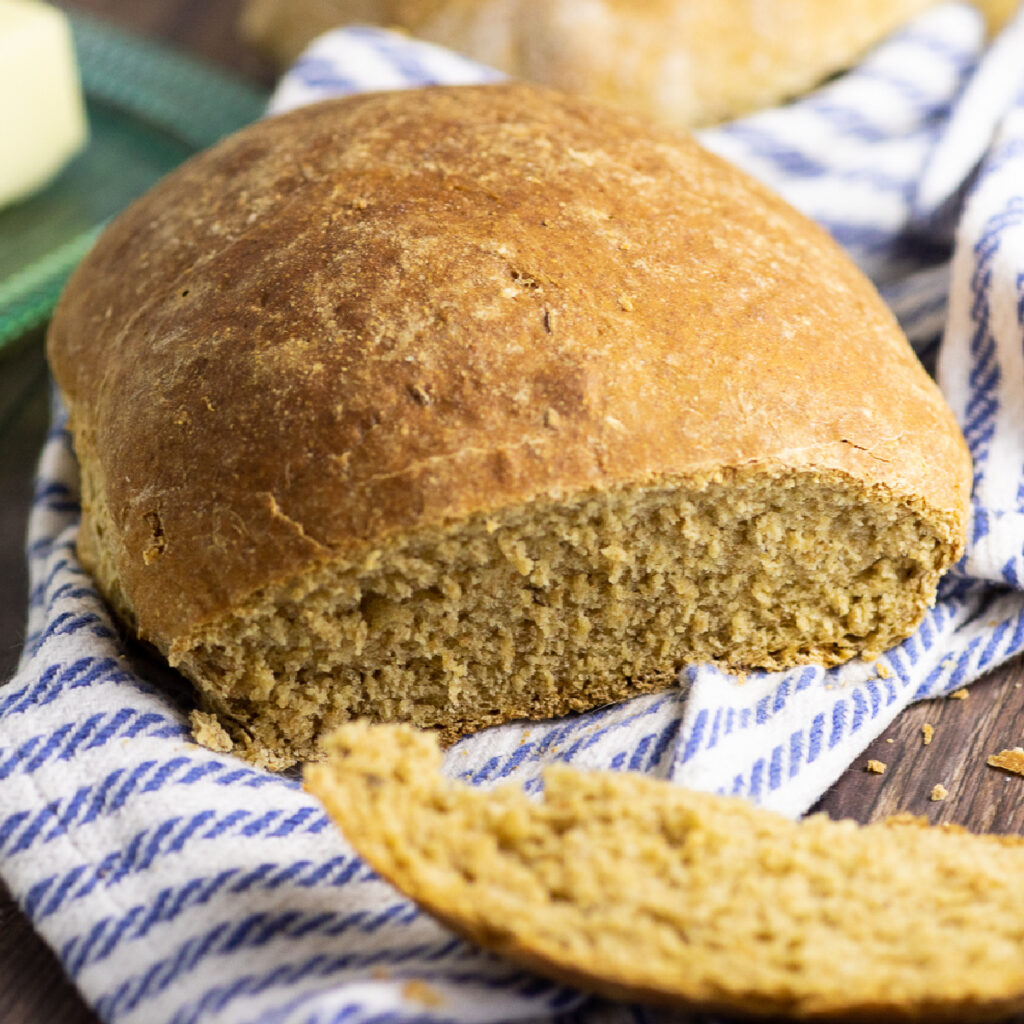 A loaf of Swedish limpa bread with a slice cut off laying in the front on a striped linen napkin.