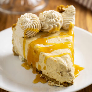 A slice of no bake pumpkin cheesecake topped with a caramel drizzle on a small white plate on a rustic wood background.