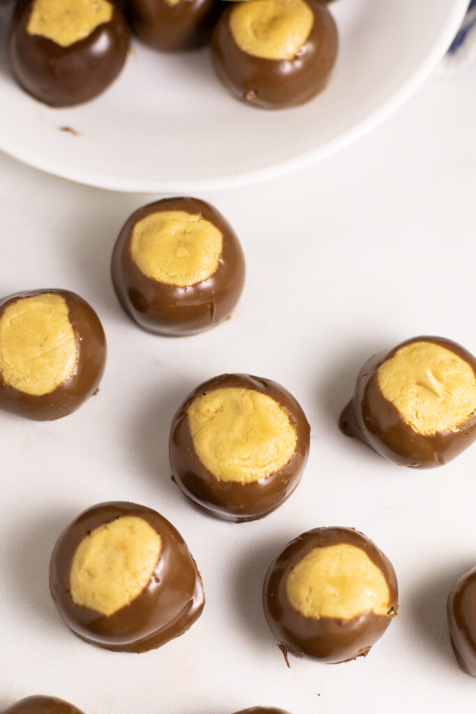 Overhead view of peanut butter buckeyes on a white marble surface with a plate with more near the top.