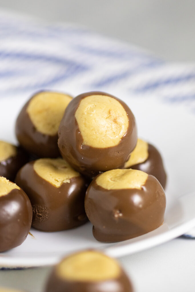 A pile of peanut butter buckeyes on a small white plate with a linen napkin in the background.