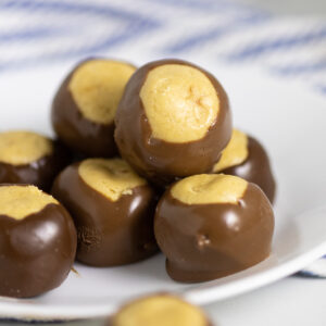 A pile of peanut butter buckeyes on a small white plate with a linen napkin in the background.