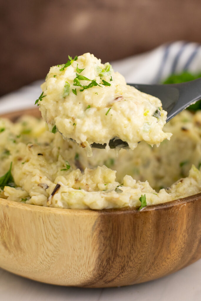 A silicone spoon taking a scoop out of a wooden bowl full of traditional colcannon.