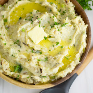 Overhead view of colcannon in a wooden bowl on a white marble surface next to a wooden spoon.