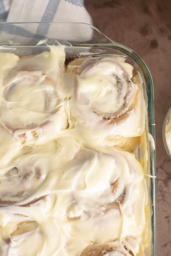Overhead view of homemade cinnamon rolls in a glass baking dish topped with cream cheese frosting.