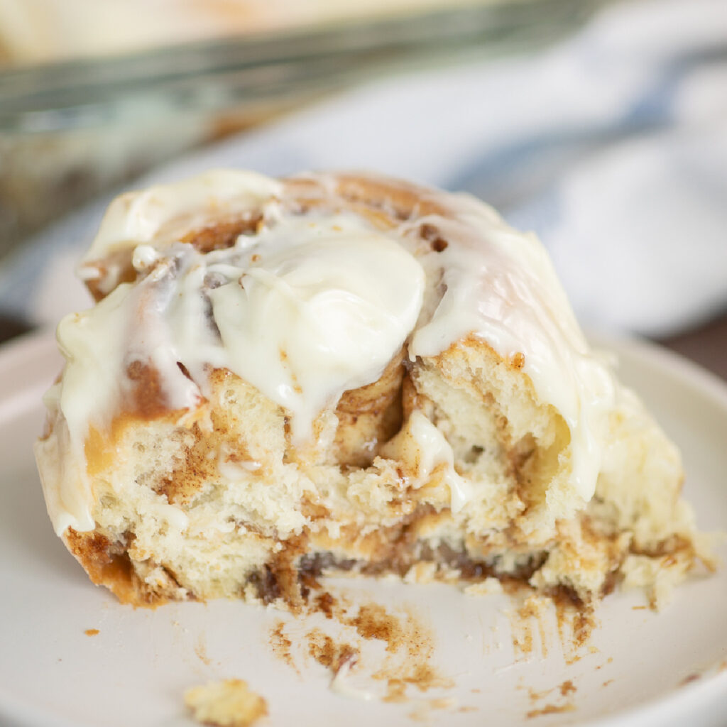 A cinnamon roll on a plate topped with cream cheese frosting, missing a bite.