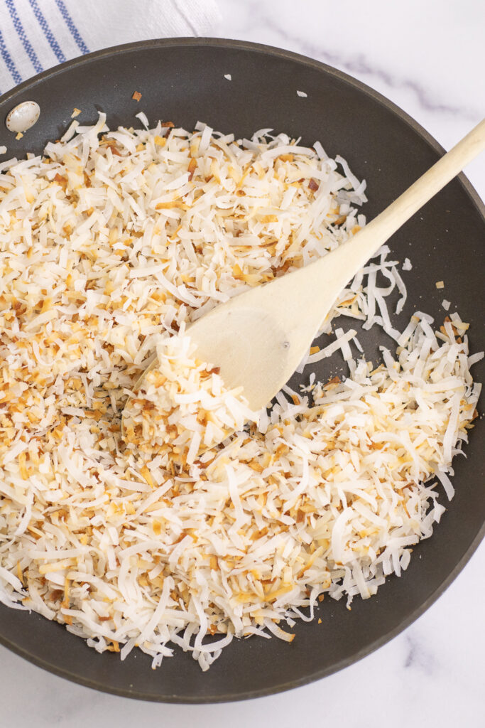 Toasted coconut in a black skillet with a wooden spoon in the center.