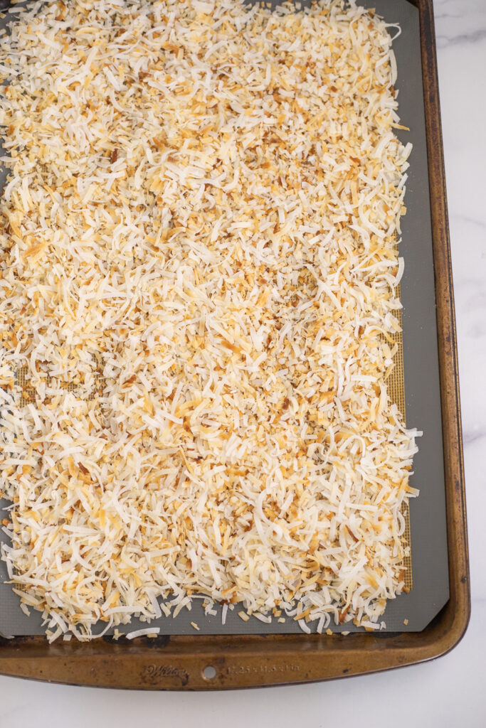 Toasted coconut on a baking sheet lined with a silicone mat.