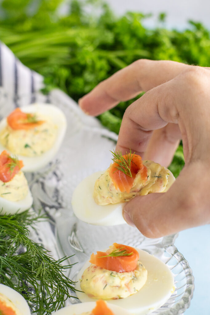 A smoked salmon deviled egg being lifted up from a deviled egg plate with a bunch of fresh parsley in the background.