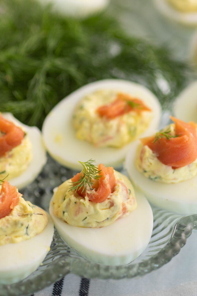 Close up of a smoked salmon deviled egg topped with smoked salmon and fresh dill next to other deviled eggs and fresh dill.