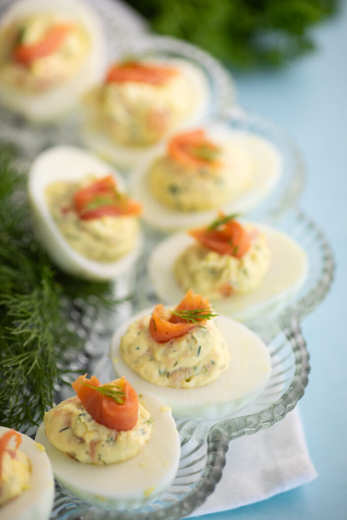 Smoked salmon deviled eggs topped with a piece of cold smoked salmon and a sprig of fresh dill on a deviled egg plate next to fresh dill.