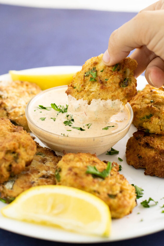 Air fryer crab cake being dipped into a small bowl of remoulade sauce.
