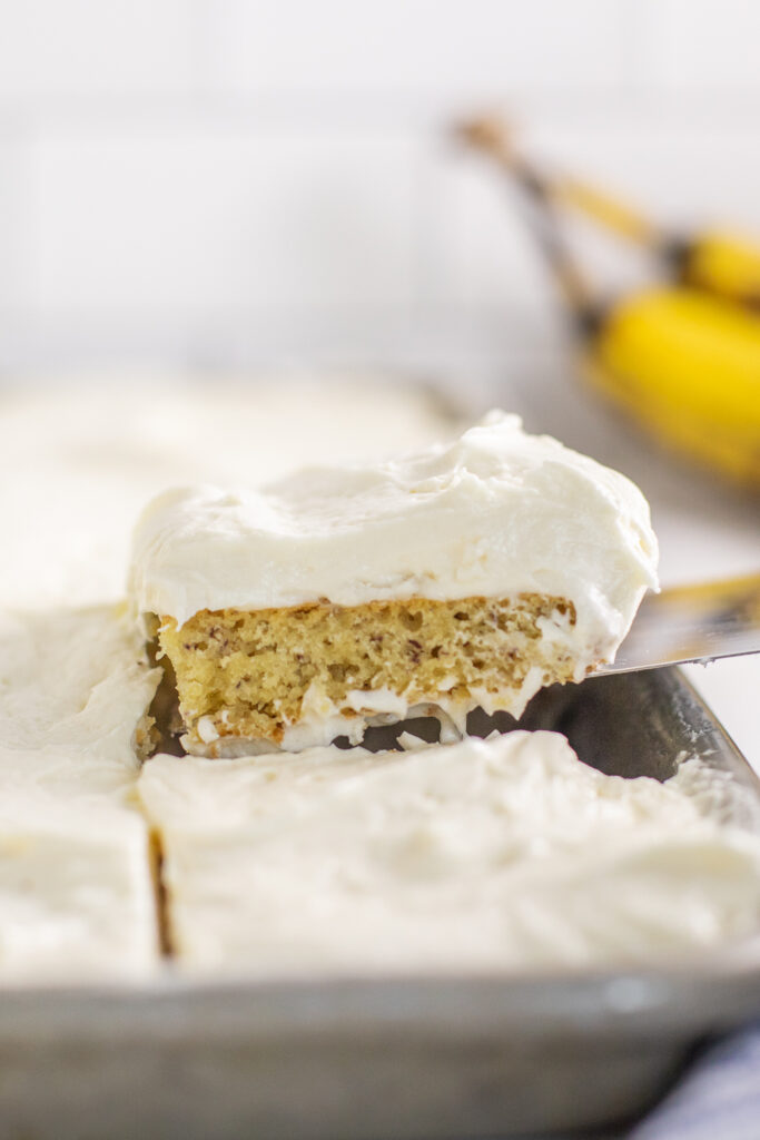 Banana bar with cream cheese frosting being lifted off the baking sheet with a spatula.