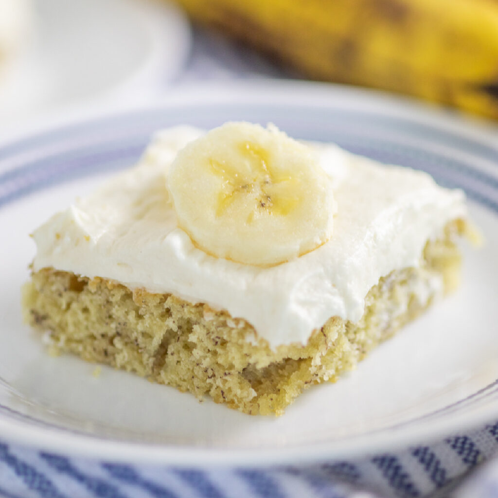 A banana bar with cream cheese frosting topped with a fresh banana slice on a small plate.