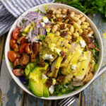 Overhead view of honey mustard chicken salad with fresh greens, avocado slices, beans, red onions, chicken, and homemade honey mustard drizzled on top.