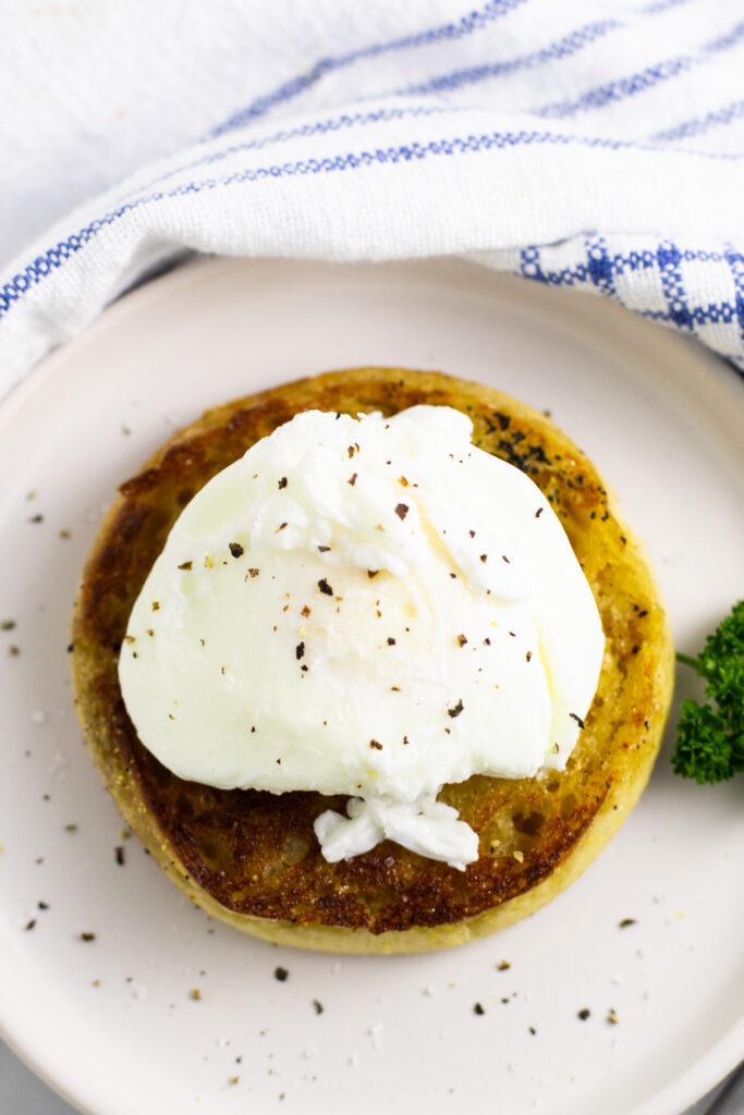 Overhead view of a microwave poached egg on half of an English muffin next to a sprig of parsley on a small ceramic plate.
