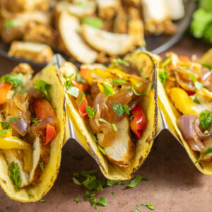 Three tacos filled with Instant Pot chicken fajita filling with chicken, bell peppers, and onions and topped with freshly chopped cilantro on a rustic background.