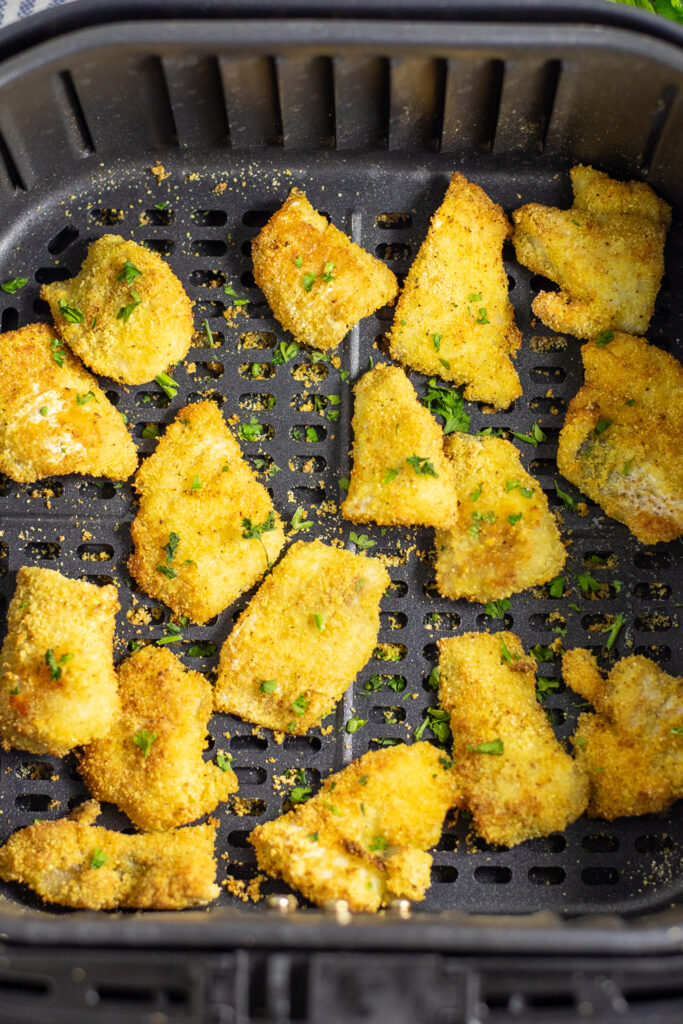 Overhead view of cornmeal breaded catfish nuggets in the basket of an air fryer.