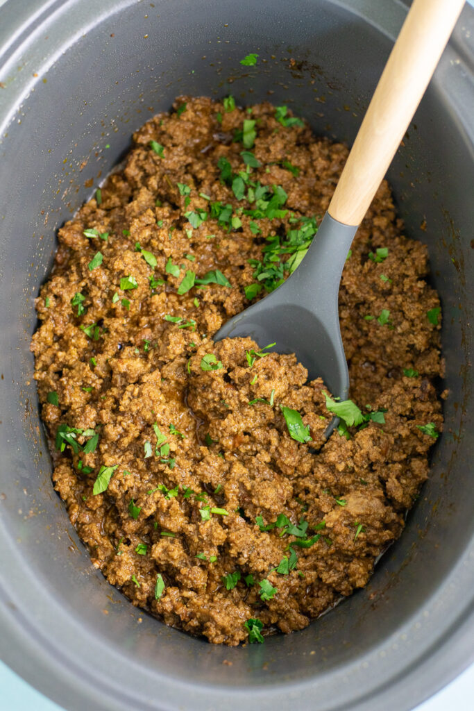 Crockpot taco meat in a slow cooker topped with fresh cilantro with a wooden spoon in the middle.