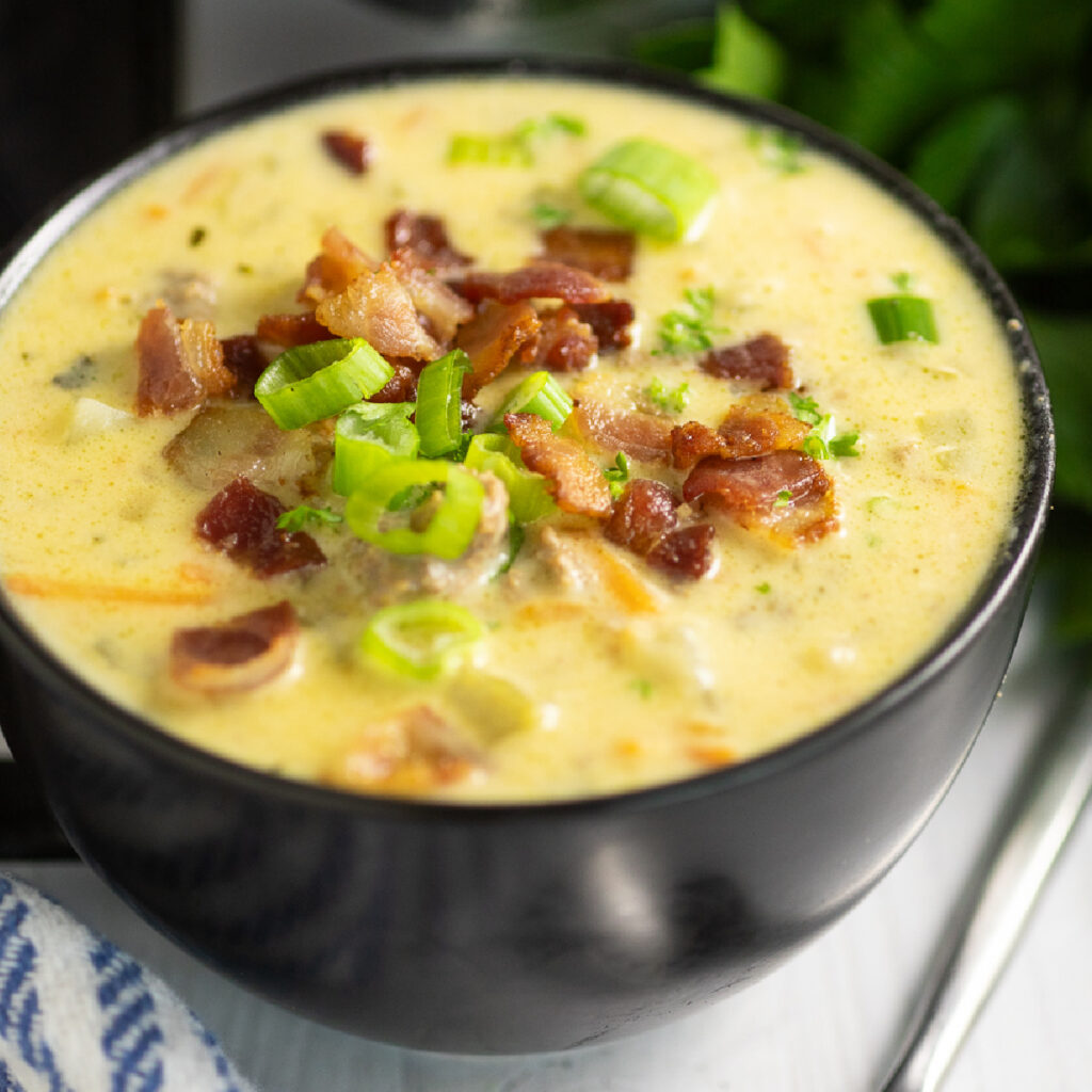 Slow Cooker Cheeseburger Soup in a black matte bowl topped with crumbled bacon and sliced green onions.
