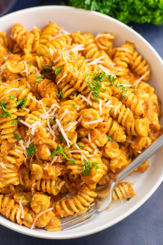 Overhead view of romesco pasta in a white matte pasta bowl with a fork in it topped with manchego cheese and fresh parsley.