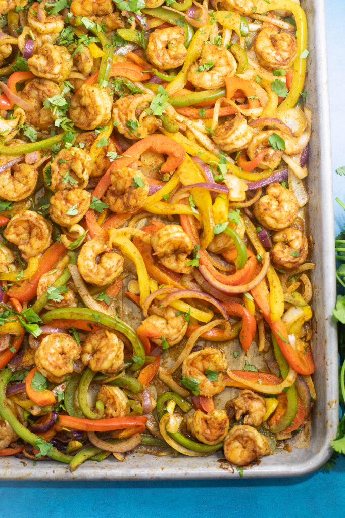 Overhead view of a sheet pan lined with parchment paper and loaded with shrimp, bell pepper strips, and onion.