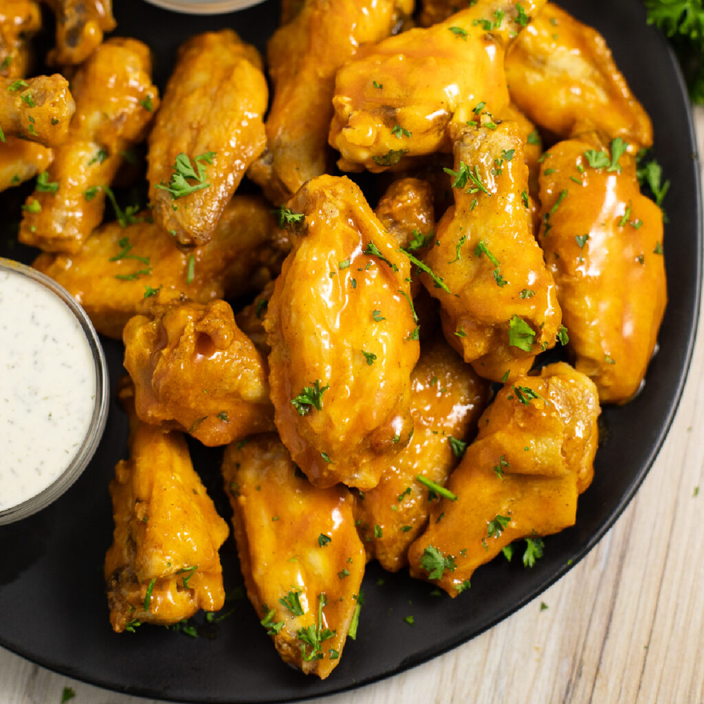 Air Fryer chicken wings coated in buffalo sauce in a pile on a matte black plate.