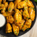 Air Fryer chicken wings coated in buffalo sauce in a pile on a matte black plate.