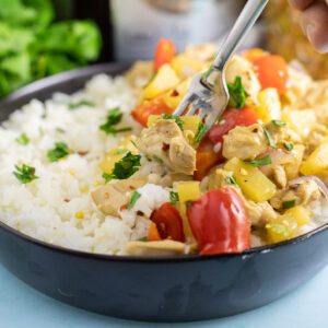 A fork taking a bite out of a bowl of crockpot pineapple chicken topped with fresh cilantro.