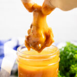 Chicken wing drumette dipping into a jar of homemade buffalo sauce.