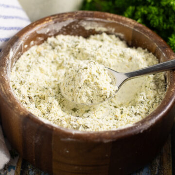 Homemade ranch seasoning in a wooden bowl with a spoon holding a scoop.