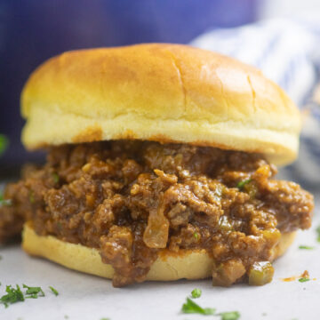 Homemade sloppy joe on a toasted bun in front of a blue pot.