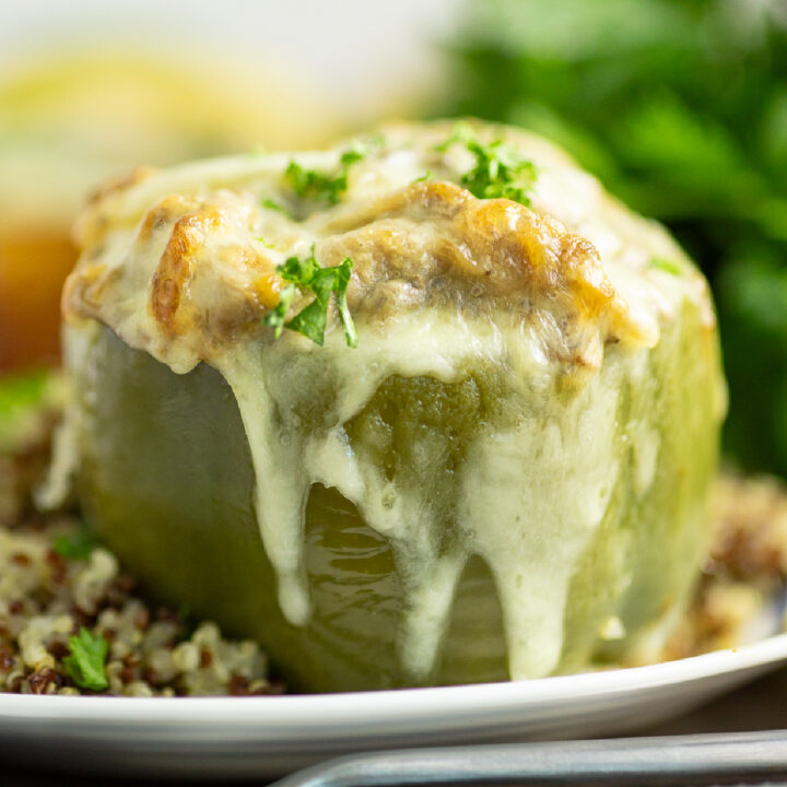 Philly cheesesteak stuffed pepper on a small plate topped with melted provolone and freshly chopped parsley next to quinoa with a bunch of fresh parsley behind.