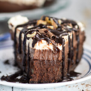 A front view of a slice of Mississippi mud pie topped with chocolate sauce and chocolate curls with a bite missing from the front, showing the layers of the pie.