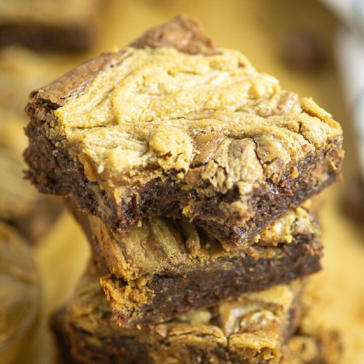 A stack of peanut butter swirl brownies on brown parchment paper with the top one with a bite taken out.