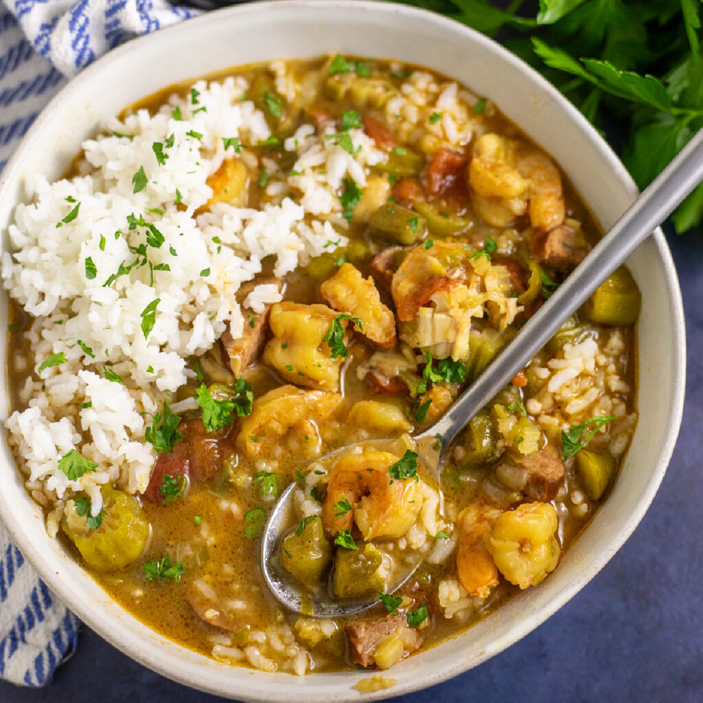 Overhead view of authentic Creole gumbo in a shallow bowl with white rice and a spoon in the middle.