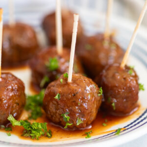 Crockpot grape jelly meatballs on a small plate with toothpicks sticking on the top, sprinkled with fresh chopped parsley.